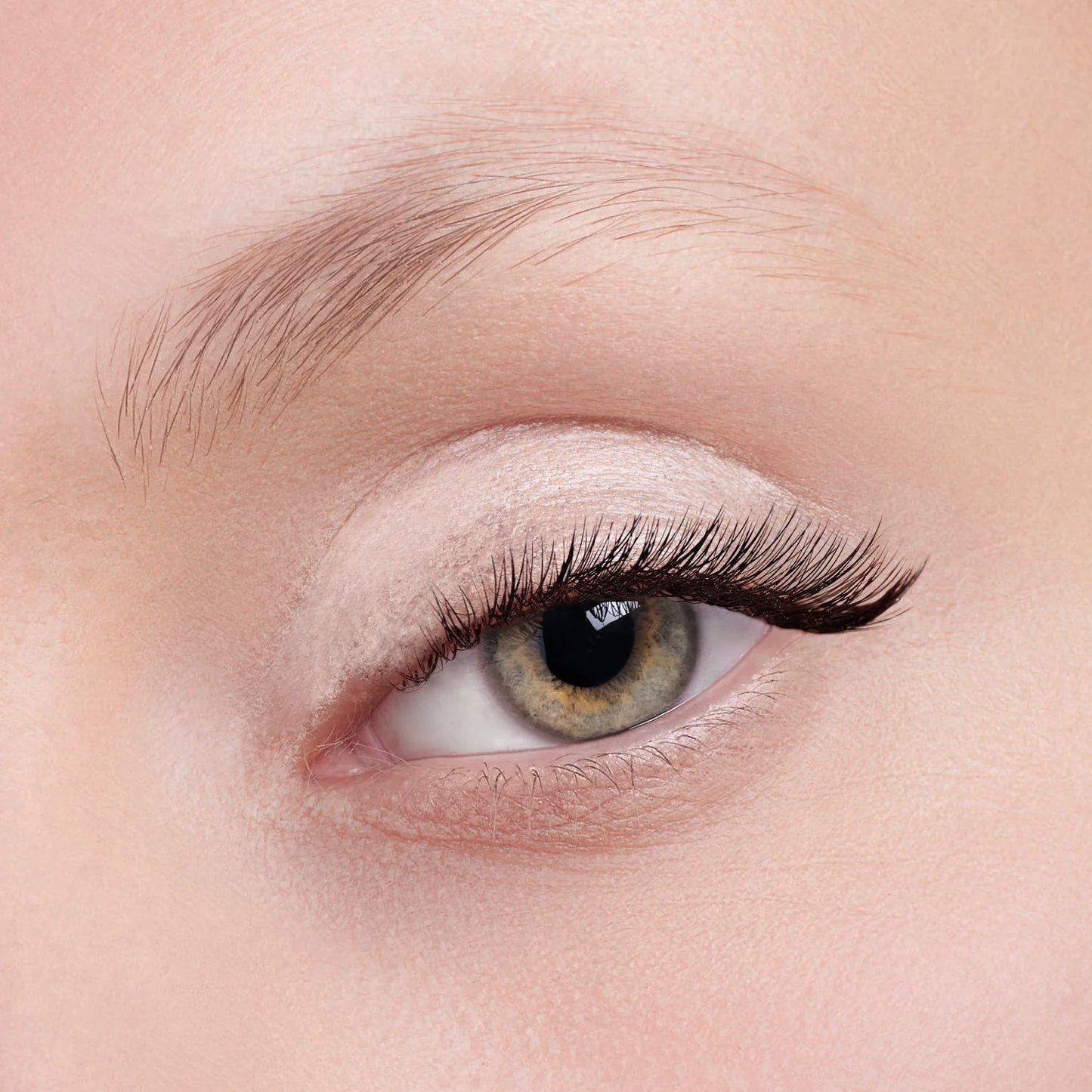 Eine Nahaufnahme des Auges einer Person mit natürlichem Make-up, langen geschwungenen Wimpern und leicht definierten Augenbrauen. Auf dem Augenlid befindet sich Flüssiger Lidschatten (3 Farbvarianten) für ein schimmerndes Finish.