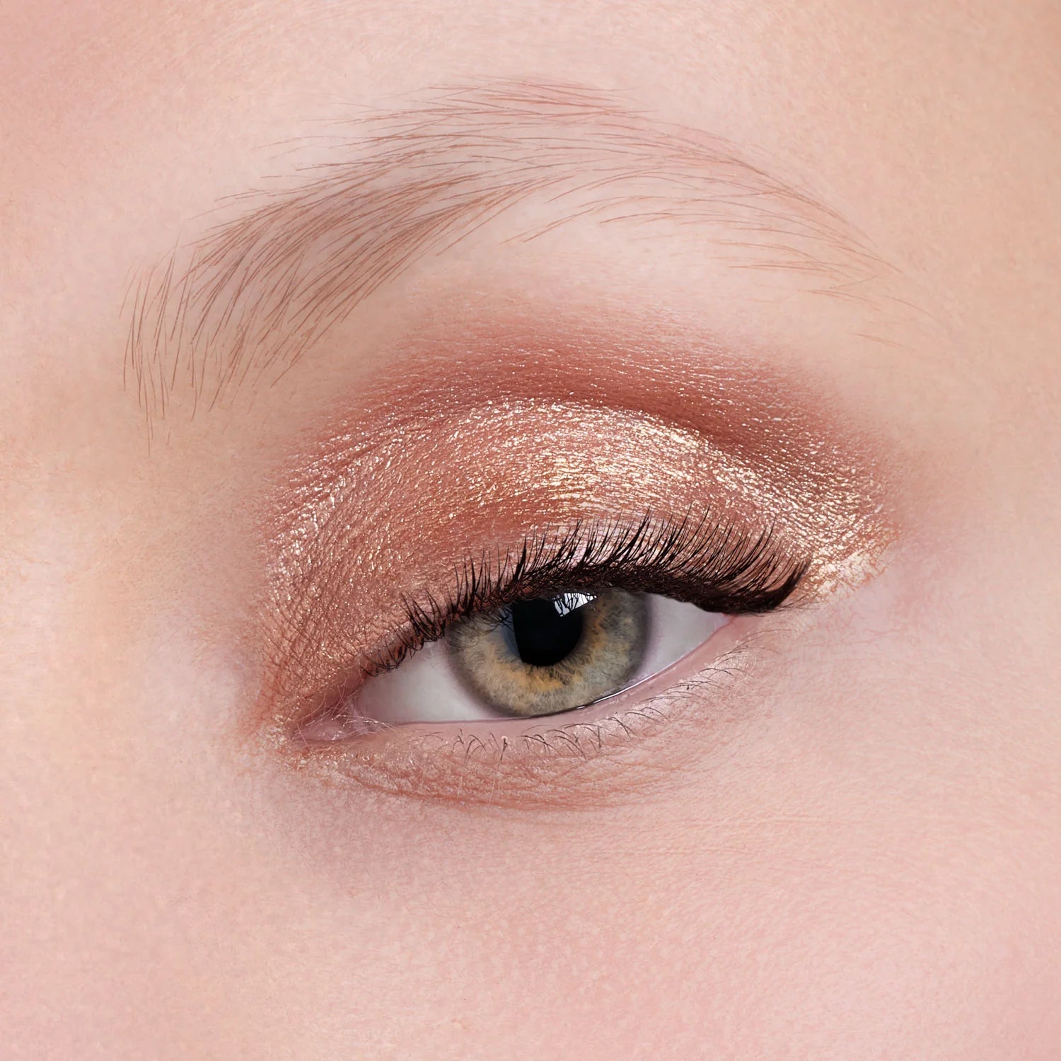 Nahaufnahme eines Auges mit hellgrüner Iris, mit Flüssiger Lidschatten (3 Farbvarianten) in schimmerndem Rosegold-Finish und schwarzer Wimperntusche, darüber eine ausgeprägte Augenbraue.