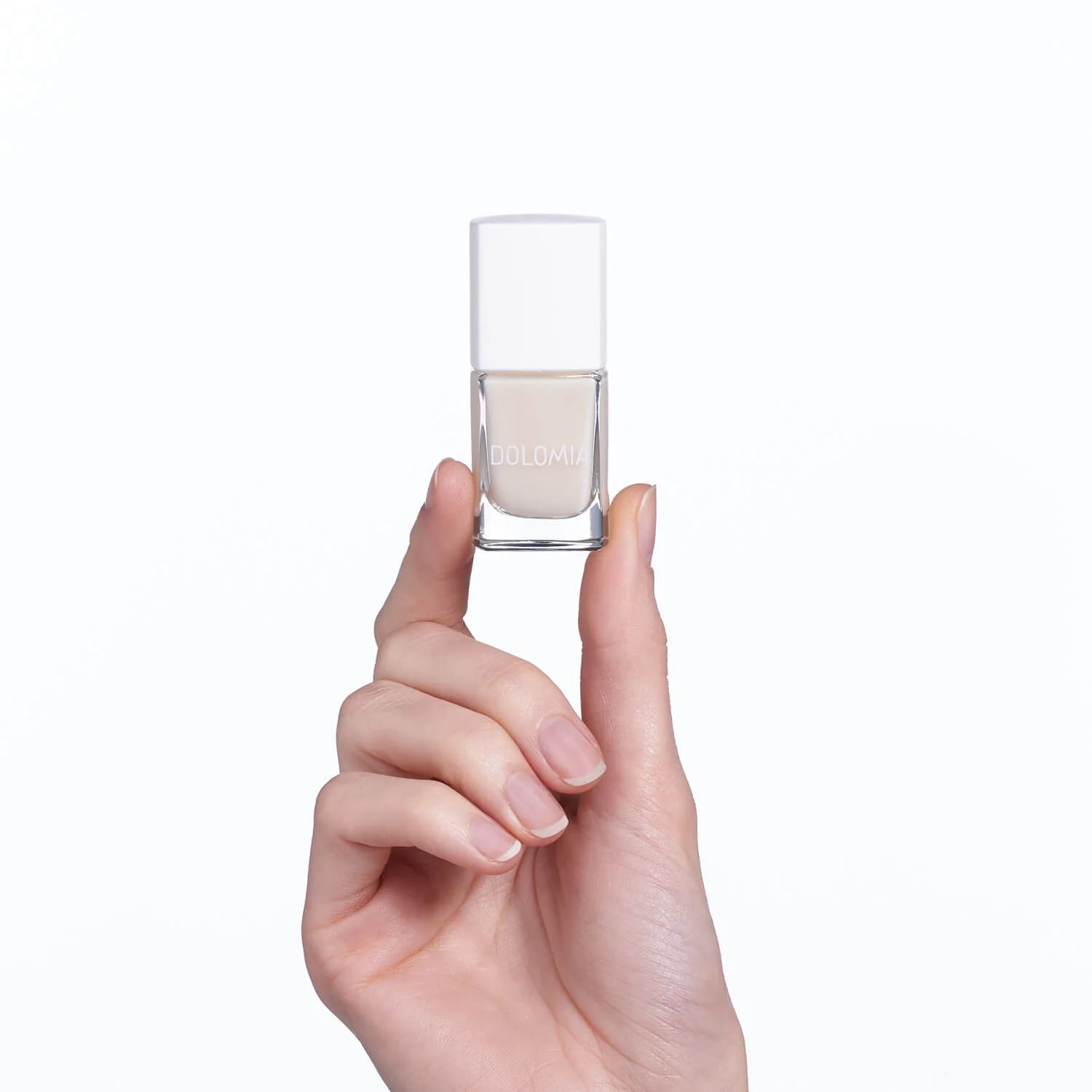 Eine gepflegte Hand hält eine kleine Flasche Stärkende Nagellackbasis, einen hellen, neutralen Nagellack, vor einem weißen Hintergrund - ideal für brüchige Nägel und perfekt als stärkende Nagellackbasis.