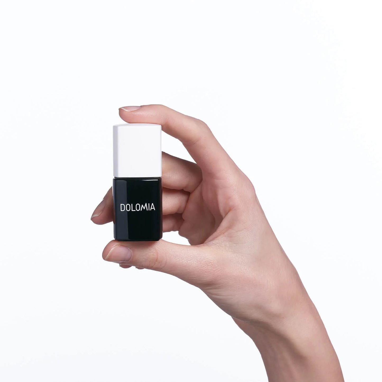 Eine Hand mit hellem Hautton hält ein kleines schwarzes Fläschchen Top Coat UV von DOLOMIA, das für zusätzliche Haltbarkeit des Nagellacks sorgt, vor einem schlichten weißen Hintergrund.