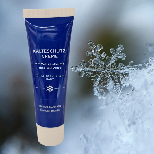 Eine blaue Tube Hinterland Apotheke Kälteschutz-Creme mit weißem Schriftzug steht neben einem Eiskristall und Schnee, hervorgehoben durch eine winterliche Kulisse, die den Kälteschutz betont.