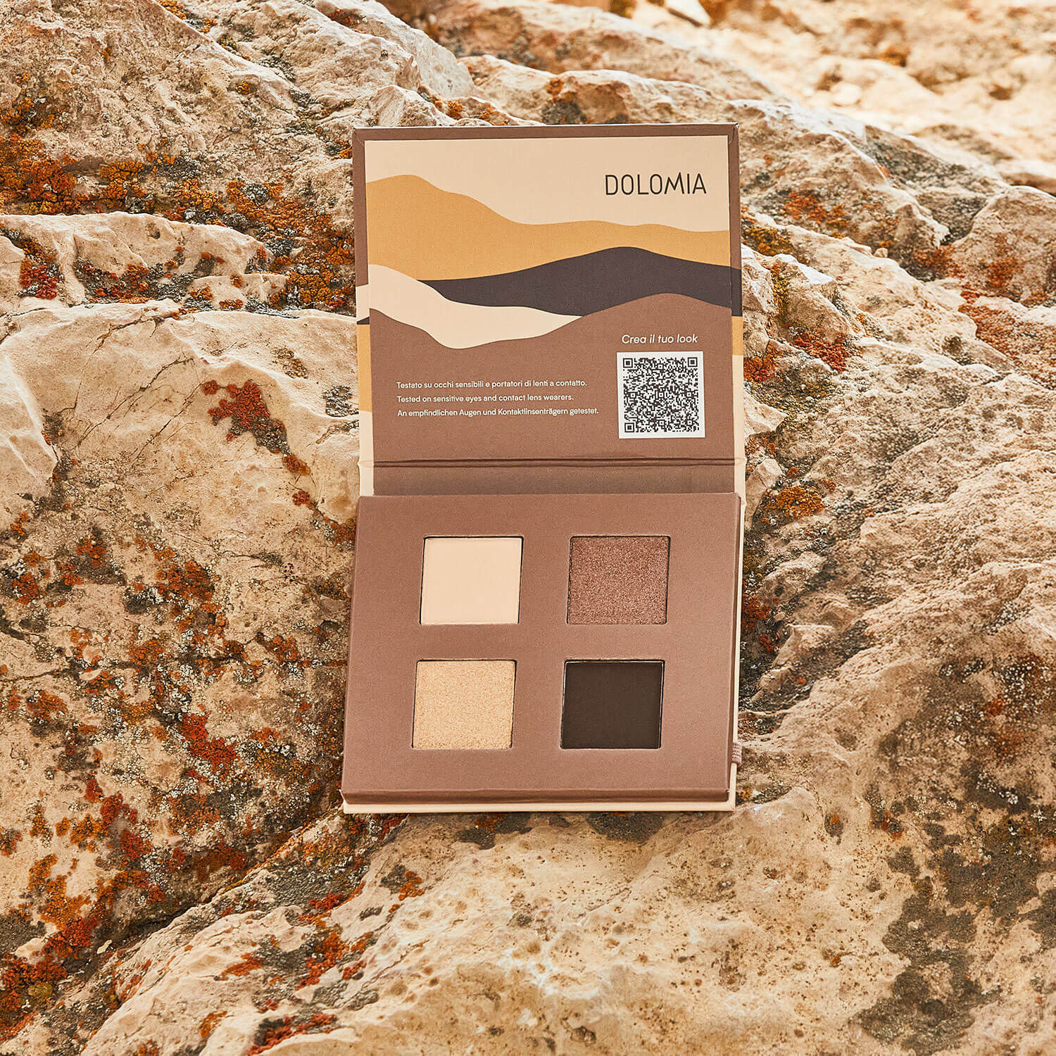 Die Natural Lidschattenpalette Chalet mit vier Brauntönen liegt offen auf strukturiertem Stein. Ihre Verpackung zeigt abstrakte Bergkunst und enthält einen QR-Code im Deckel - natürliche Eleganz in Perfektion.