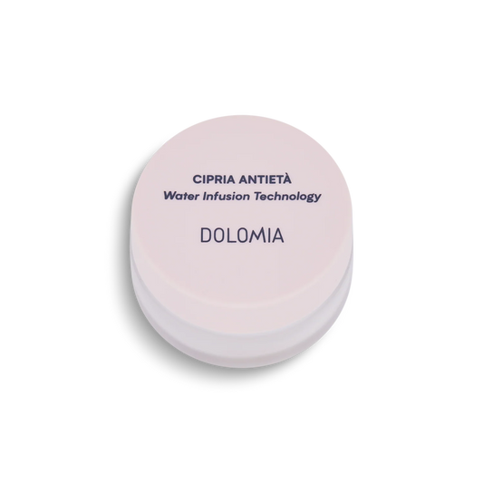 Ein runder, hellrosa Kosmetikbehälter mit der Aufschrift Anti-Aging Puder mit Water Infusion Technology und Edelweiß-Extrakt für einen makellosen Teint, von oben gesehen auf weißem Hintergrund.