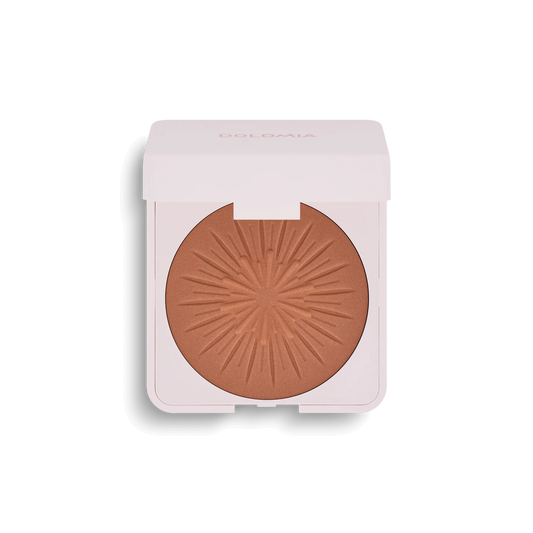 Bräunungspuder ist ein kompakter Bronzer mit gepresstem Puder im Sonnenschliff-Design, untergebracht in einem weißen, quadratischen Etui mit Scharnierdeckel. Auf dem Deckel ist dezent der Markenname DOLOMIA zu sehen.
