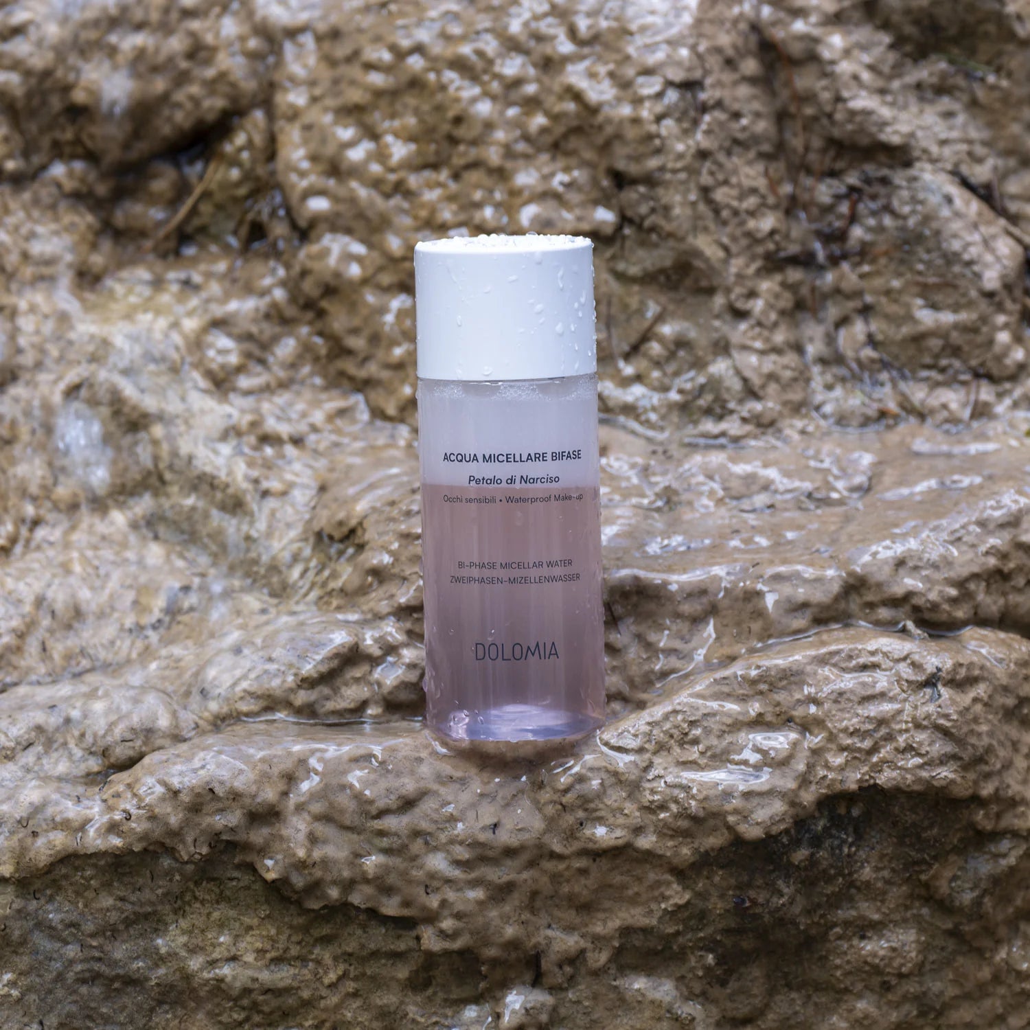Eine Flasche Zweiphasen-Mizellenwasser Narzissenextrakt sitzt auf nassen, strukturierten Felsen mit Wassertropfen und schafft eine frische, natürliche Szene, die ideal für empfindliche Haut ist.