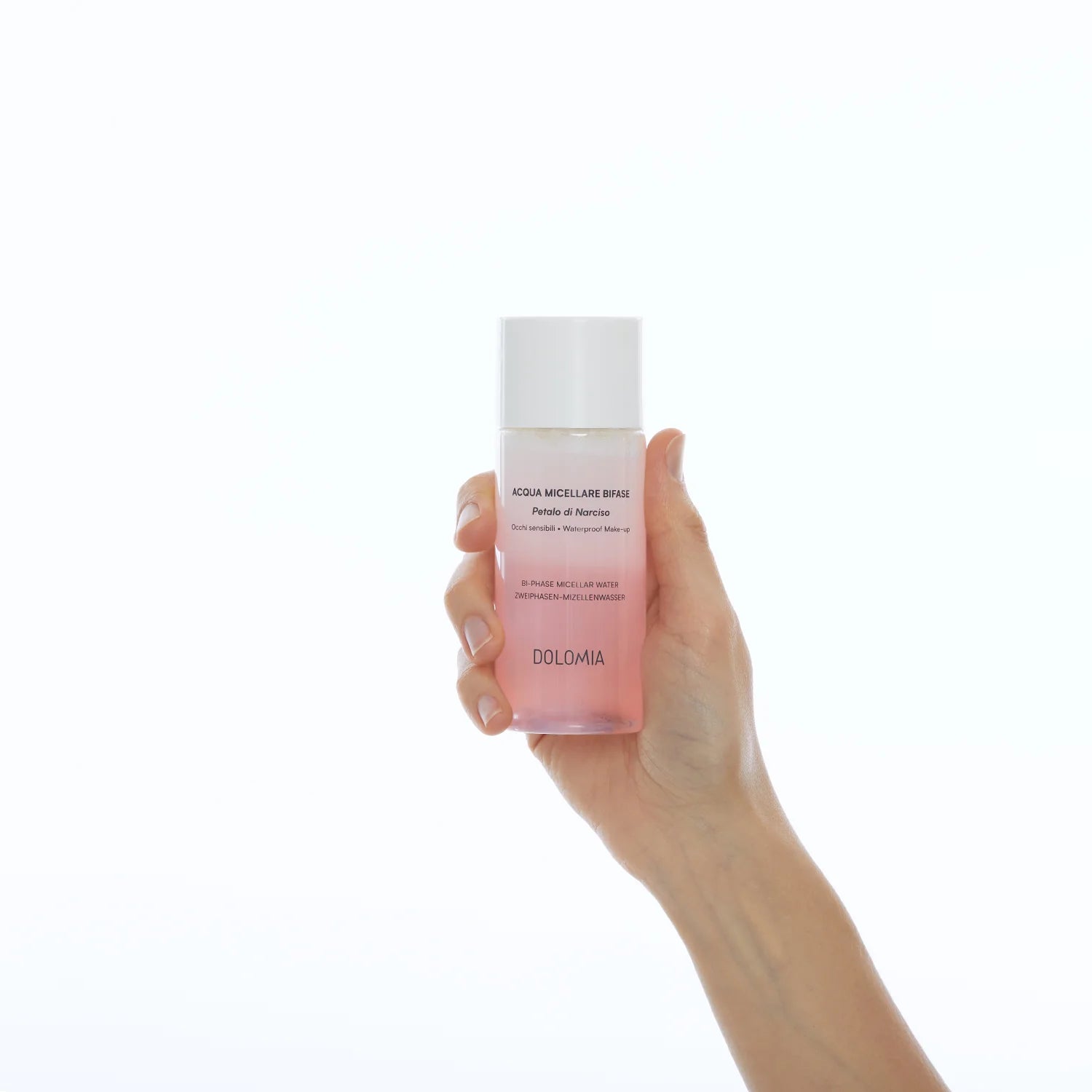 Eine Hand hält eine klare Flasche rosa Zweiphasen-Mizellenwasser Narzissenextrakt, ein idealer Make-up-Entferner für empfindliche Haut, vor einem schlichten weißen Hintergrund.