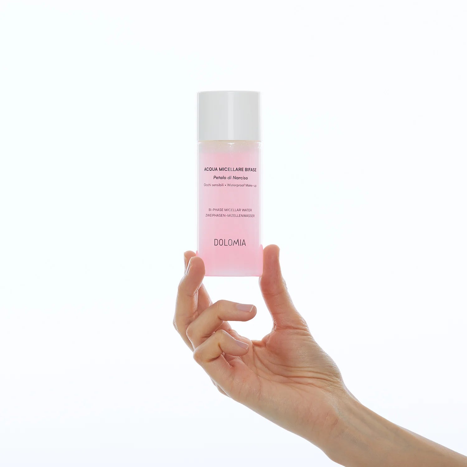 Eine Hand hält eine durchsichtige Flasche mit rosafarbener Flüssigkeit mit der Aufschrift Zweiphasen-Mizellenwasser Narzissenextrakt, ideal für empfindliche Haut, vor einem schlichten weißen Hintergrund hoch.