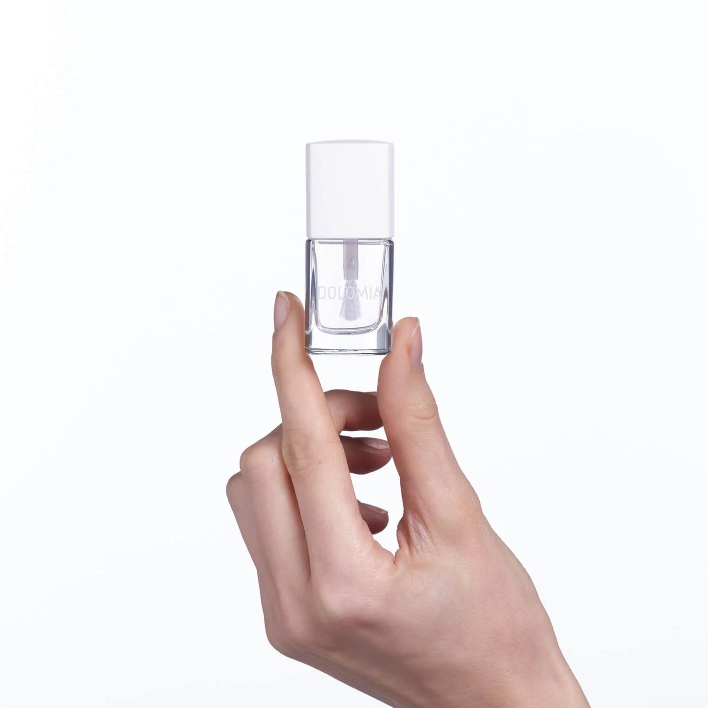 Eine Hand mit ordentlich manikürten, brüchigen Nägeln hält eine kleine durchsichtige Flasche Repair SOS-Nagellackbasis mit α-Hydroxysäuren und einer weißen Kappe vor einem schlichten weißen Hintergrund.