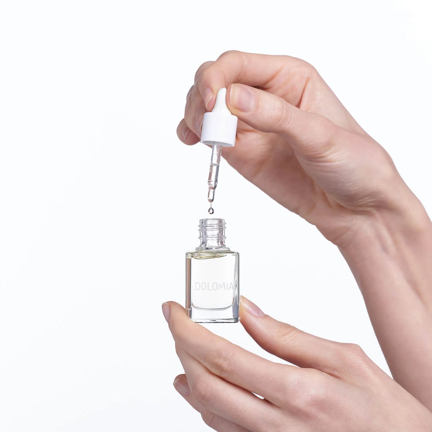 Eine Person hält ein kleines Glasfläschchen Natürliches Pflegeöl mit der Aufschrift DOLOMIA in der Hand und trägt mit einer Pipette einen Tropfen zur sanften Nagelpflege auf. Der Hintergrund ist einfarbig weiß.