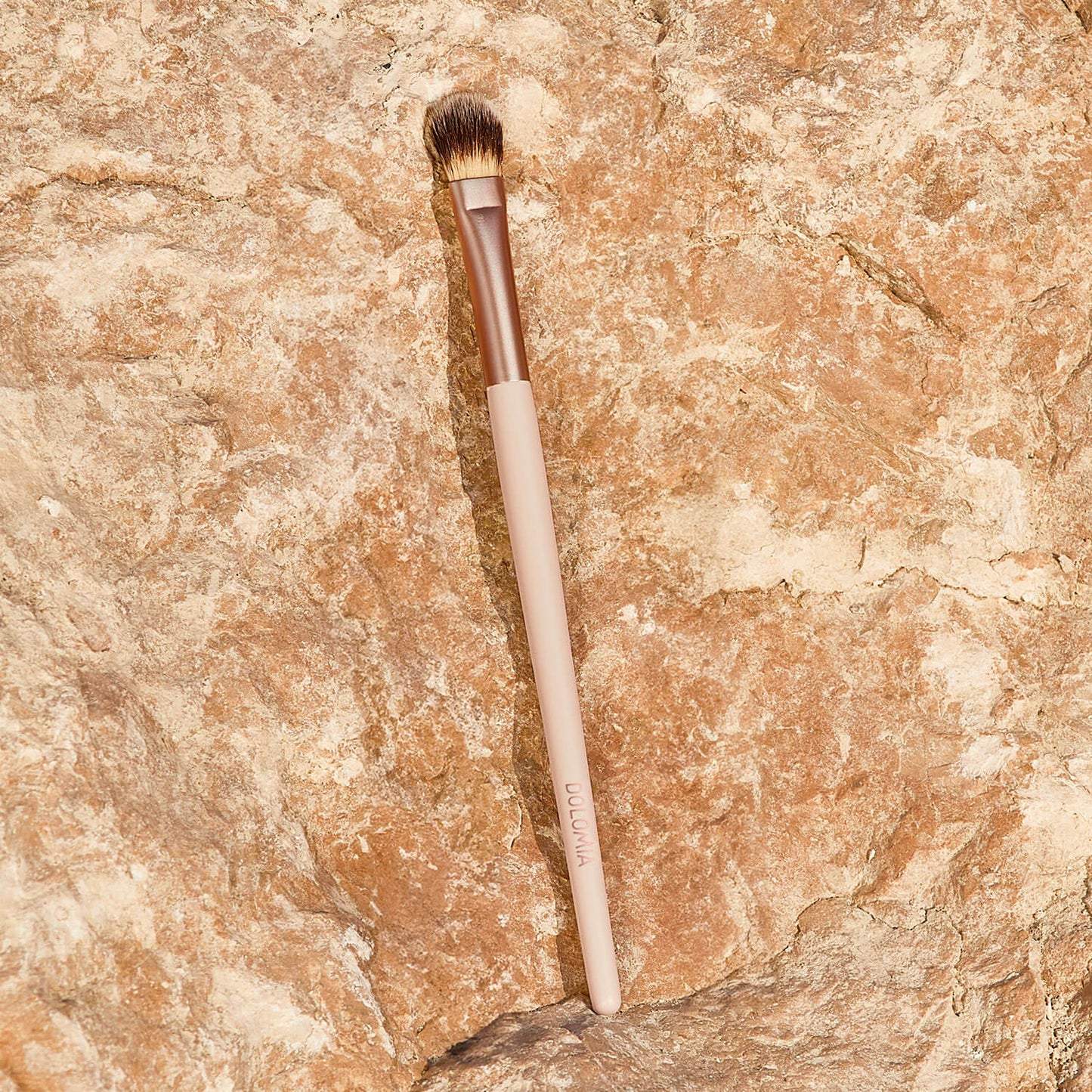 Der Augenpinsel für Schattierungen mit beige-farbenem Griff und braunen, synthetischen Fasern liegt auf einer texturierten, hellbraunen Steinoberfläche.