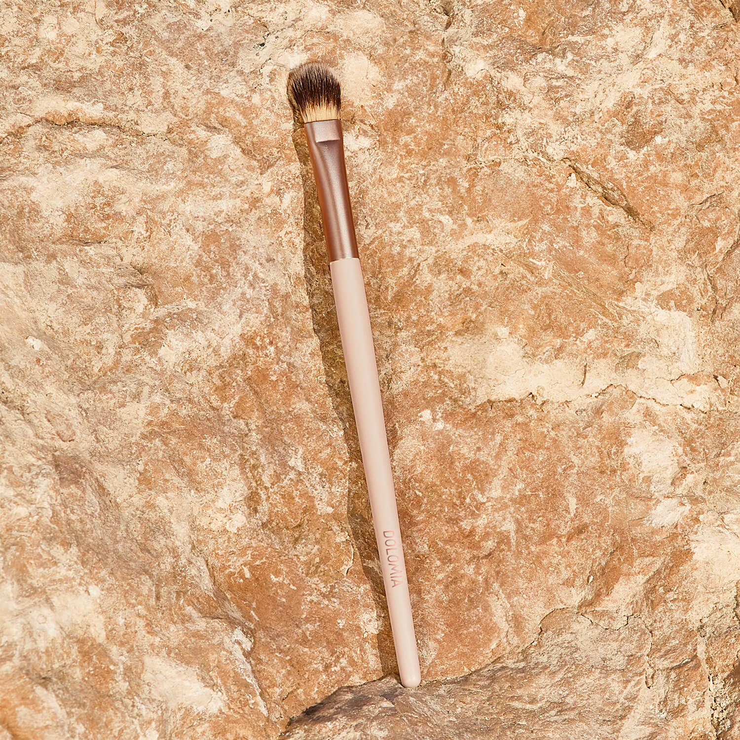 Der Augenpinsel für Schattierungen mit beige-farbenem Griff und braunen, synthetischen Fasern liegt auf einer texturierten, hellbraunen Steinoberfläche.