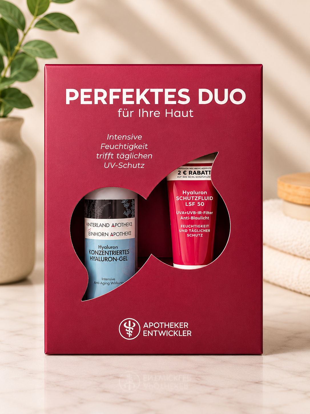 Eine Schachtel mit der Aufschrift "Perfektes Duo - Konzentriertes Hyaluron-Gel + Hyaluron Schutzfluid LSF 50" ist auf einer hellen Fläche mit einer Blattpflanze im Hintergrund ausgestellt.